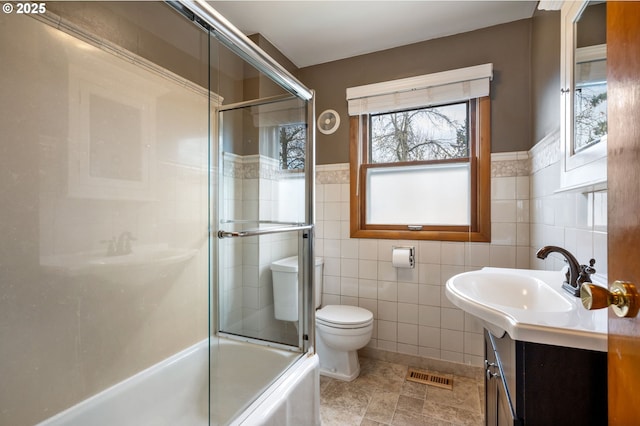 bathroom with visible vents, toilet, enclosed tub / shower combo, vanity, and tile walls