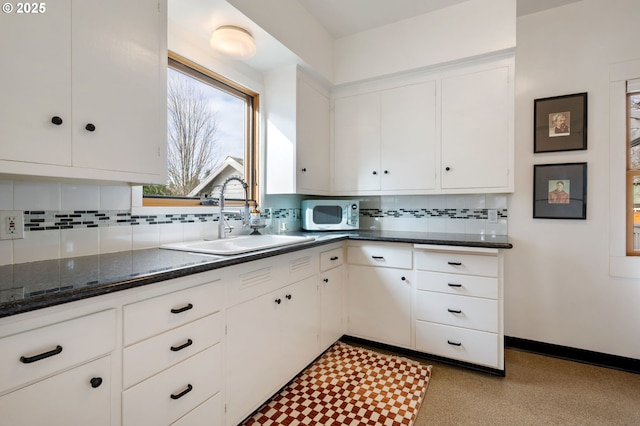 kitchen featuring stainless steel microwave, backsplash, white cabinets, a sink, and baseboards