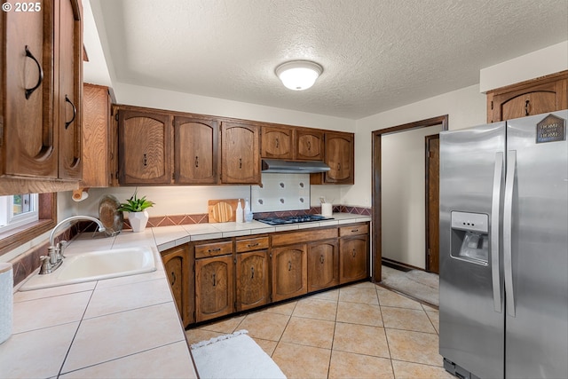 15648 NE Rose Pkwy, Portland, OR 97230 - kitchen with stainless steel fridge, tile countertops, under cabinet range hood, a sink, and black gas cooktop