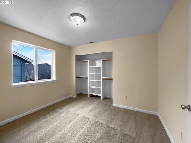 unfurnished bedroom with a closet, visible vents, carpet flooring, a textured ceiling, and baseboards