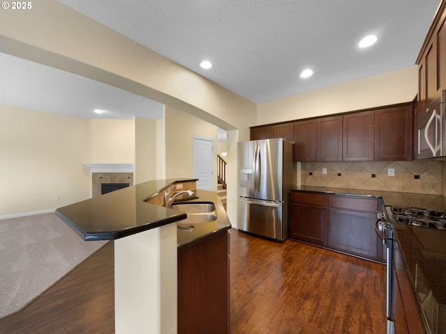 kitchen with a tiled fireplace, dark countertops, appliances with stainless steel finishes, open floor plan, and a sink