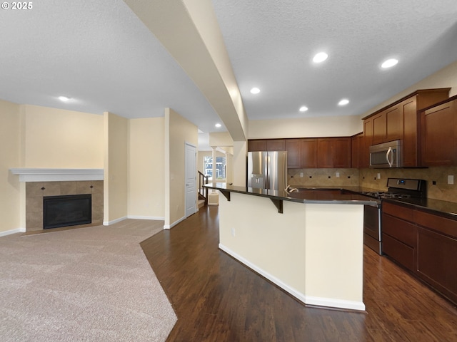 kitchen featuring dark countertops, appliances with stainless steel finishes, a kitchen island with sink, a kitchen bar, and backsplash