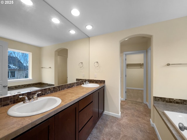 bathroom with a bath, a spacious closet, a sink, and recessed lighting