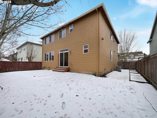 snow covered back of property with entry steps, a fenced backyard, and cooling unit