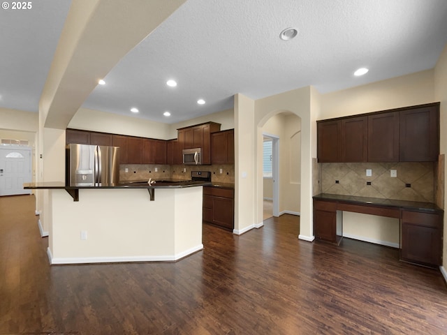 kitchen with arched walkways, dark countertops, a kitchen breakfast bar, dark wood-style flooring, and stainless steel appliances