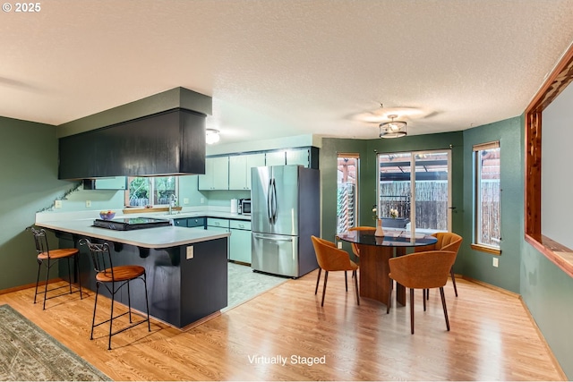 kitchen with light wood finished floors, appliances with stainless steel finishes, a peninsula, light countertops, and a sink