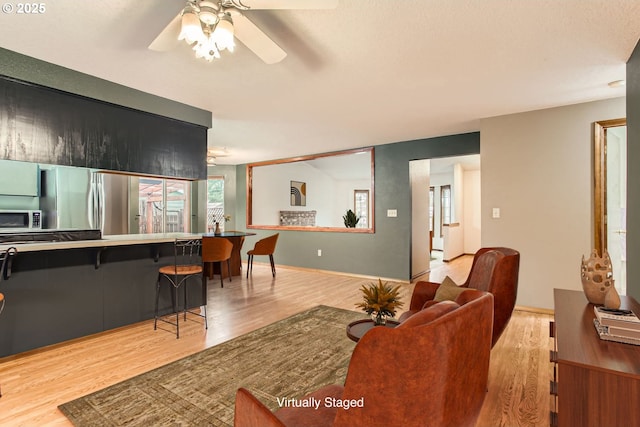 living area featuring baseboards, a ceiling fan, and light wood-style floors