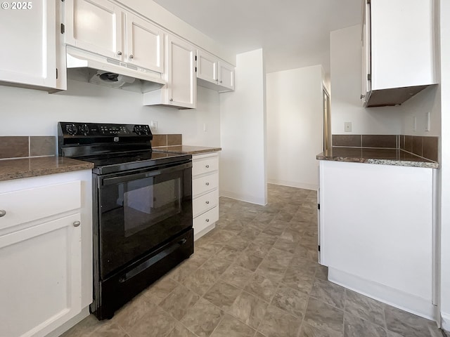 kitchen with electric range, under cabinet range hood, dark stone countertops, white cabinets, and baseboards