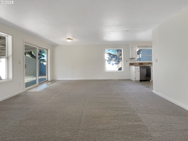 unfurnished living room with light colored carpet, a textured ceiling, and baseboards