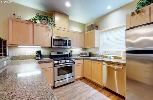 kitchen featuring light brown cabinetry, tile countertops, a sink, light wood-style flooring, and appliances with stainless steel finishes