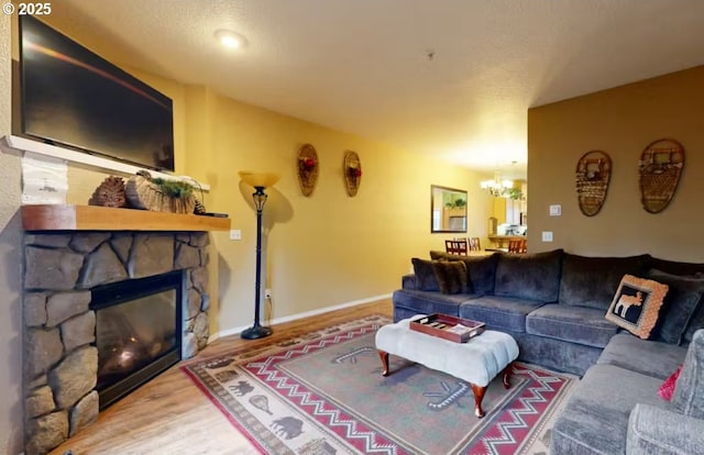 living area featuring a stone fireplace, baseboards, wood finished floors, and a chandelier