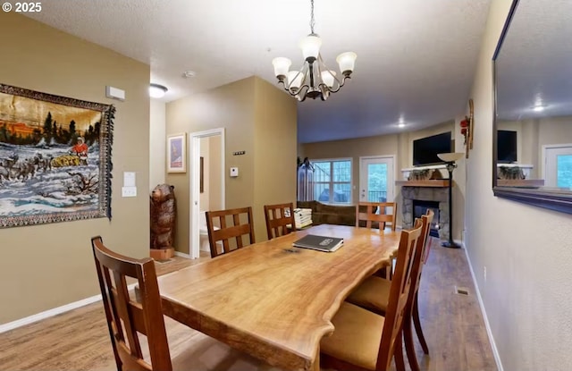 dining area with baseboards, wood finished floors, a chandelier, and a fireplace