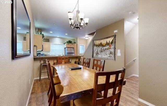 dining space with baseboards, a notable chandelier, and light wood finished floors