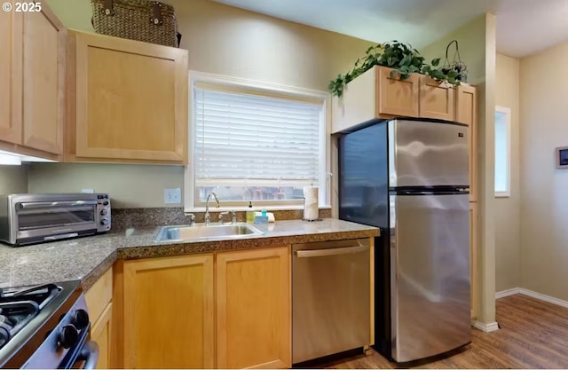 kitchen featuring light brown cabinetry, stainless steel appliances, a sink, and light wood-style flooring
