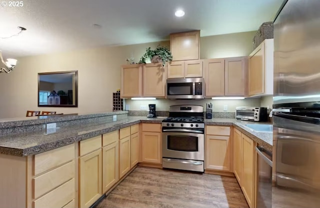 kitchen with tile countertops, light brown cabinetry, appliances with stainless steel finishes, a peninsula, and light wood-style floors