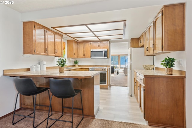 kitchen with wall oven, white refrigerator, kitchen peninsula, and a breakfast bar