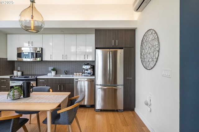1455 N Killingsworth St Unit 201, Portland, OR 97217 - kitchen with appliances with stainless steel finishes, light countertops, decorative backsplash, light wood-type flooring, and white cabinetry