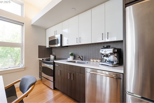 1455 N Killingsworth St Unit 201, Portland, OR 97217 - kitchen featuring appliances with stainless steel finishes, light countertops, light wood-style flooring, backsplash, and a sink