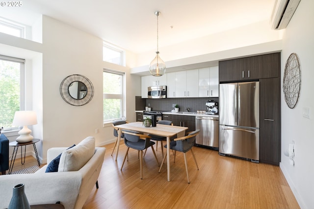 1455 N Killingsworth St Unit 201, Portland, OR 97217 - kitchen featuring appliances with stainless steel finishes, an AC wall unit, light wood finished floors, and backsplash