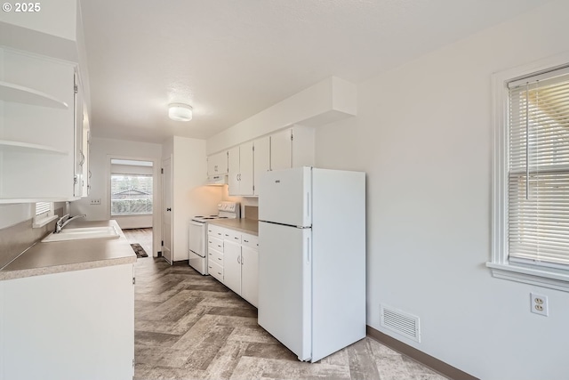 kitchen with white appliances, a sink, visible vents, white cabinetry, and light countertops