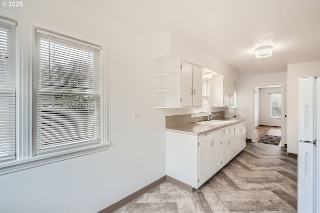 kitchen with a sink, white cabinetry, light countertops, freestanding refrigerator, and open shelves