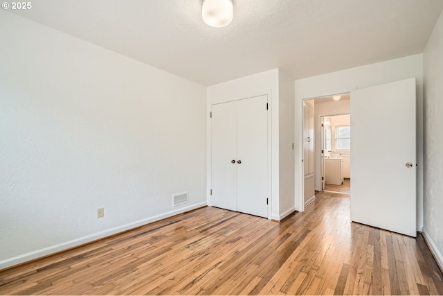 unfurnished bedroom with a closet, visible vents, light wood-style flooring, and baseboards