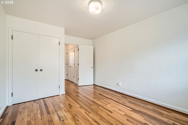 unfurnished bedroom with a textured ceiling, a closet, light wood-style flooring, and baseboards