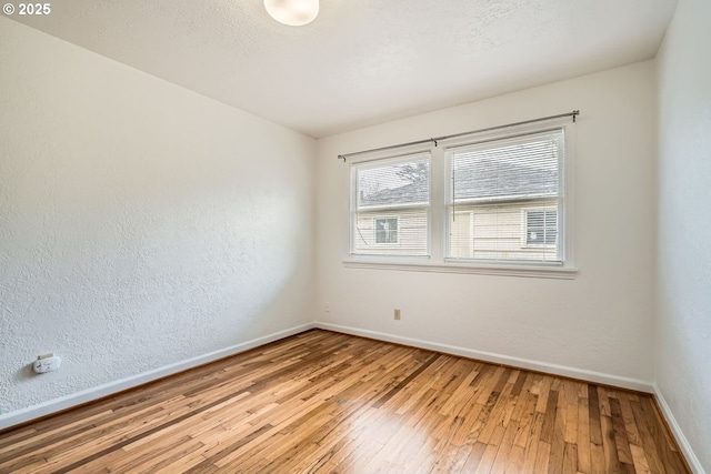 empty room with a textured wall, a textured ceiling, baseboards, and wood finished floors