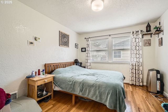 bedroom featuring a textured ceiling, a textured wall, visible vents, baseboards, and light wood-style floors