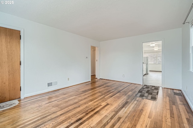 spare room with a textured ceiling, light wood-style flooring, visible vents, and baseboards