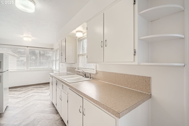 kitchen featuring white cabinets, light countertops, a textured ceiling, open shelves, and a sink