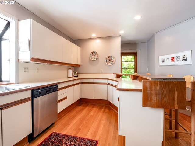 kitchen featuring light wood finished floors, dishwasher, light countertops, a peninsula, and a kitchen bar