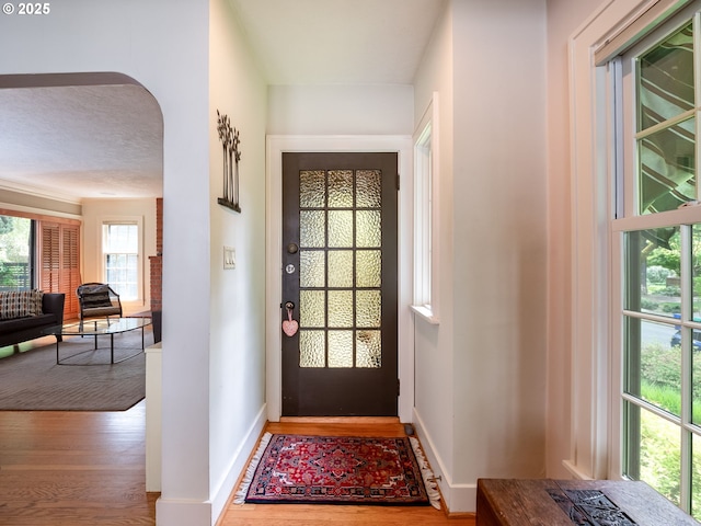doorway to outside with arched walkways, baseboards, and wood finished floors