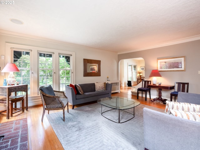 living area with arched walkways, ornamental molding, and light wood finished floors