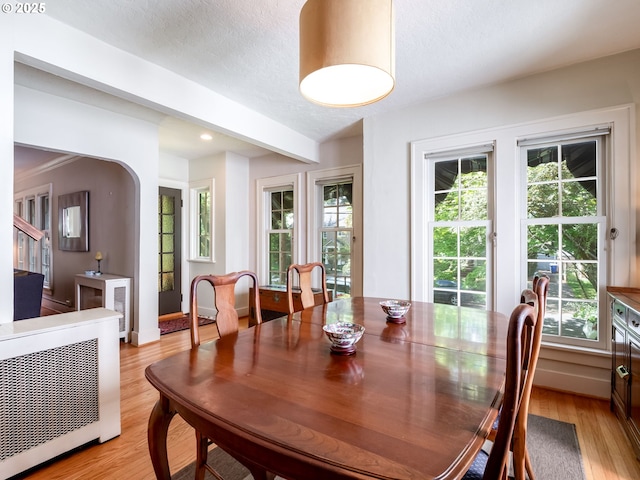 dining space featuring arched walkways, a textured ceiling, and light wood-style flooring