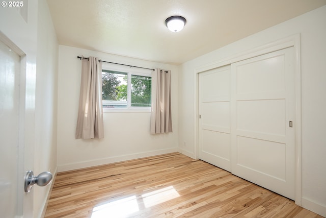 unfurnished bedroom with light wood finished floors, baseboards, and a closet