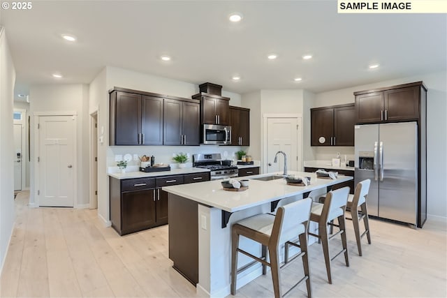 23870 SW Vermillion Dr, Tualatin, OR 97062 - kitchen featuring appliances with stainless steel finishes, a sink, a kitchen bar, light wood-style floors, and dark brown cabinetry