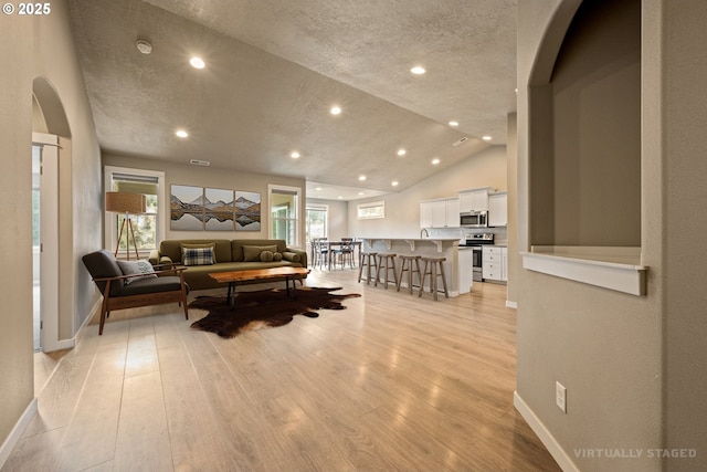 7220 SE Night Hawk Ct, Prineville, OR 97754 - living area featuring arched walkways, lofted ceiling, recessed lighting, baseboards, and light wood finished floors