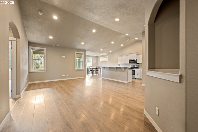 7220 SE Night Hawk Ct, Prineville, OR 97754 - unfurnished living room with arched walkways, light wood finished floors, vaulted ceiling, and baseboards