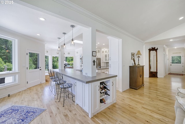 kitchen with decorative light fixtures, light hardwood / wood-style floors, white cabinetry, and vaulted ceiling