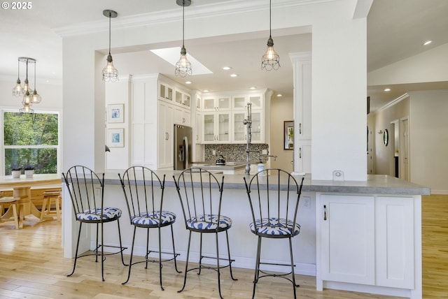 kitchen with kitchen peninsula, white cabinets, tasteful backsplash, and stainless steel fridge