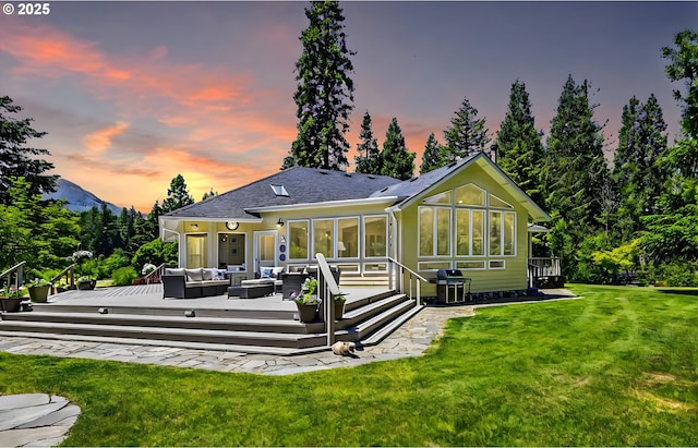 back house at dusk with a deck, outdoor lounge area, and a yard