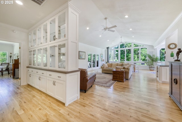 kitchen featuring high vaulted ceiling, white cabinetry, light hardwood / wood-style flooring, and crown molding