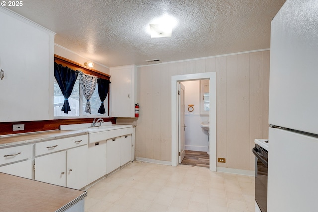 kitchen with crown molding, a textured ceiling, electric range oven, white refrigerator, and white cabinets