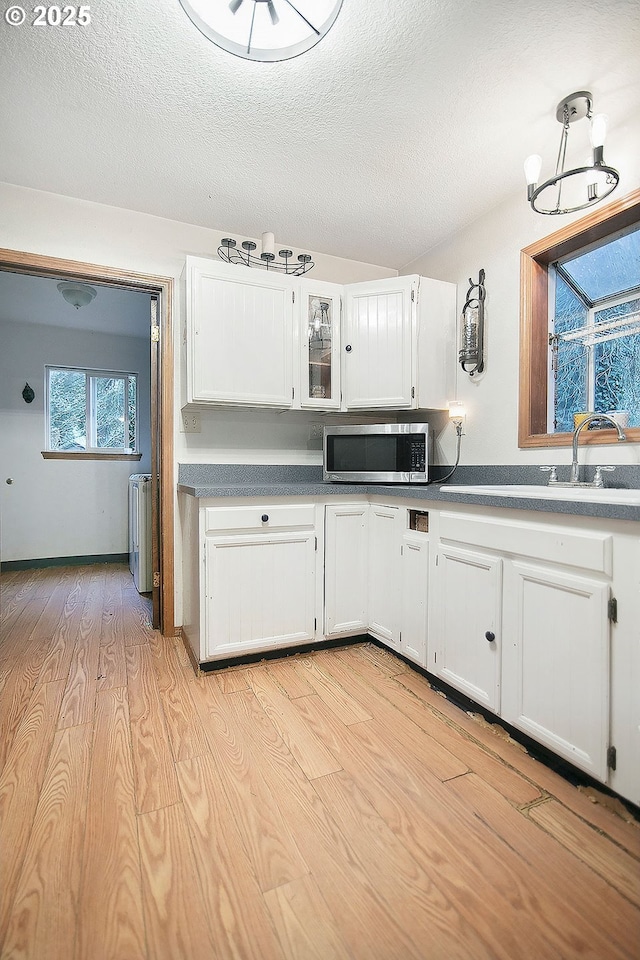 kitchen with an inviting chandelier, white cabinets, a textured ceiling, and light wood-type flooring