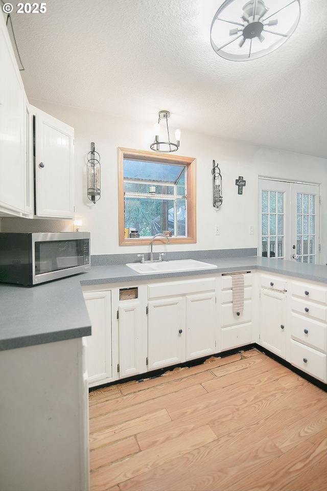 kitchen featuring sink, white cabinets, a textured ceiling, and light wood-type flooring