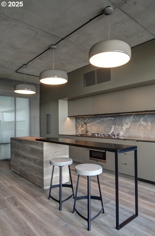 1410 NW Kearney St Unit 721, Portland, OR 97209 - bar with a sink, hanging light fixtures, decorative backsplash, light wood finished floors, and visible vents