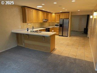 kitchen featuring brown cabinets, light colored carpet, a peninsula, and freestanding refrigerator