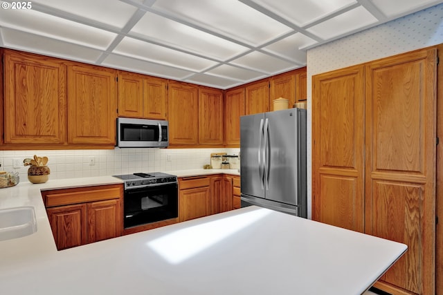kitchen featuring appliances with stainless steel finishes, decorative backsplash, light countertops, brown cabinetry, and a peninsula