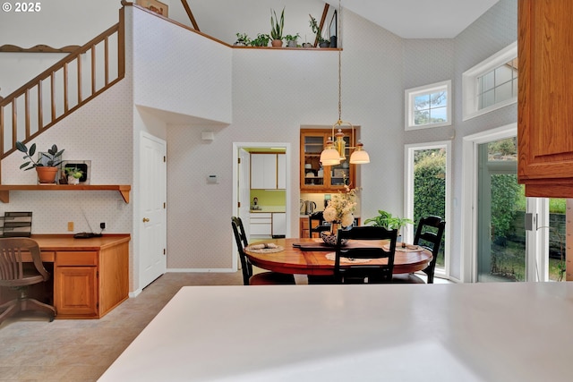dining area with wallpapered walls, an office area, a towering ceiling, stairs, and baseboards